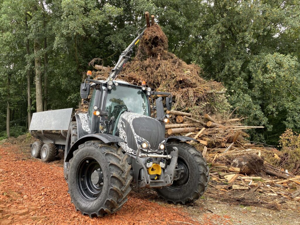 Трактор Валтра Н174 превози велики терет грања у шуми.