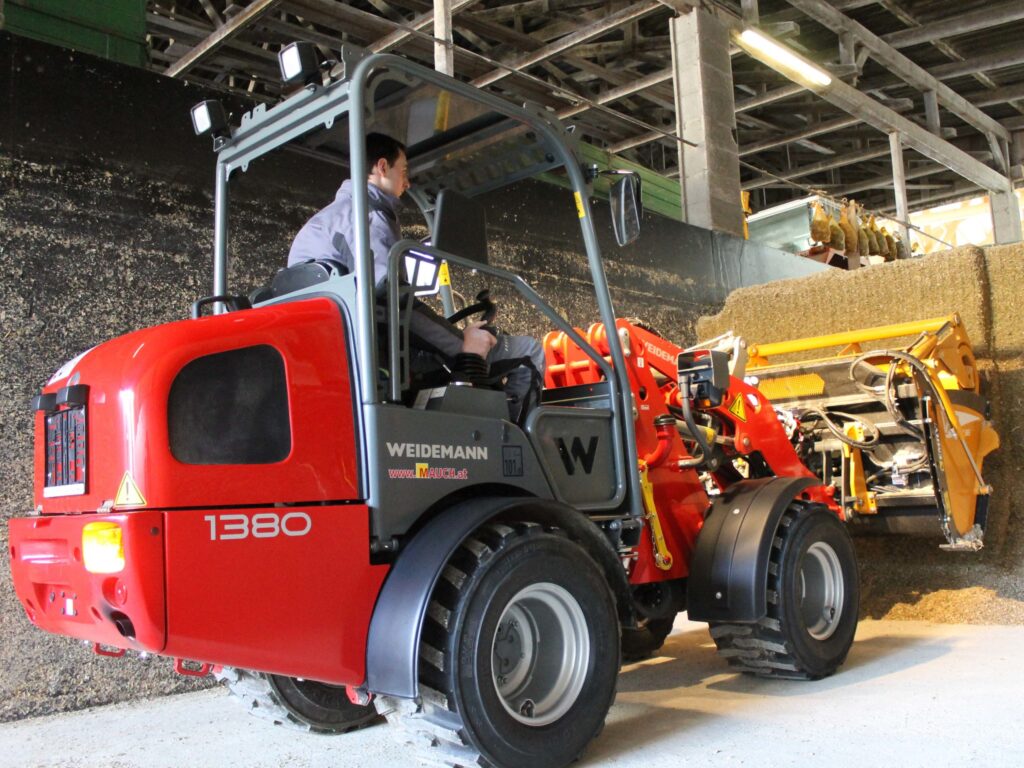 Ein roter Weidemann Radlader 1380 wird von einer Person in einer Lagerhalle gefahren.