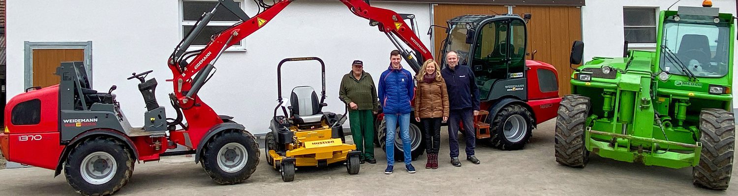 Vier Personen stehen vor verschiedenen landwirtschaftlichen Maschinen, darunter ein Hustler FasTrak SDX54.