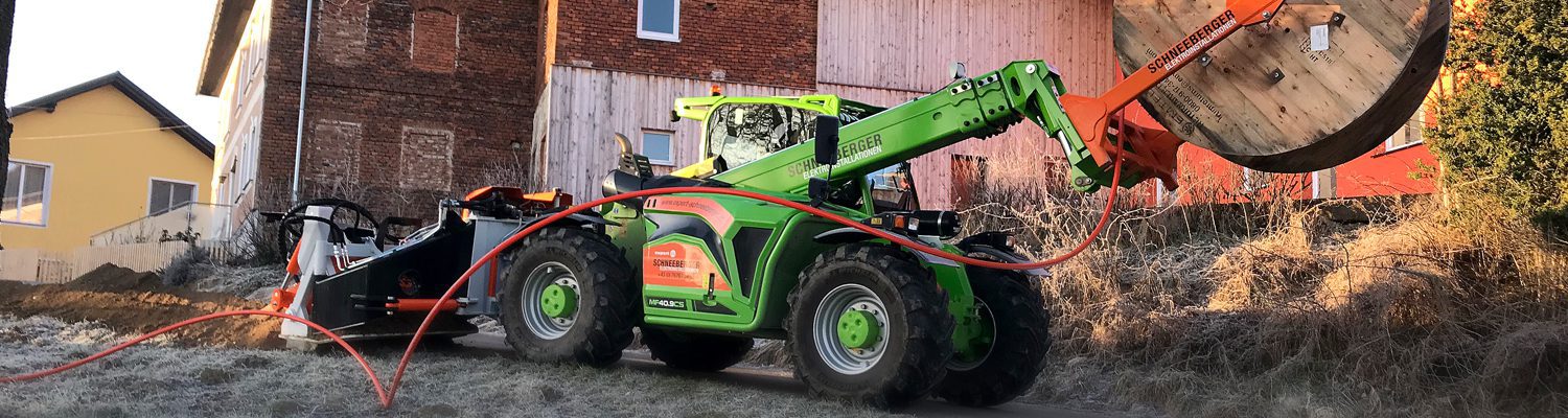 Ein Merlo MF 40.9 CS Traktor, der eine große Holzspule transportiert, vor einem Gebäude.