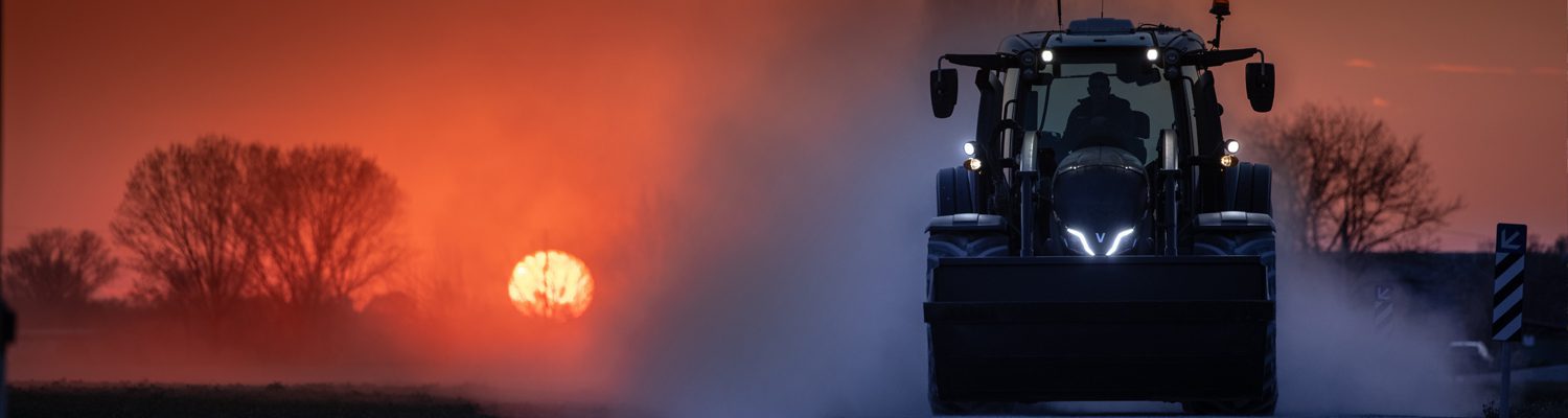 Valtra-Traktor fährt bei Sonnenuntergang durch eine staubige Landschaft.