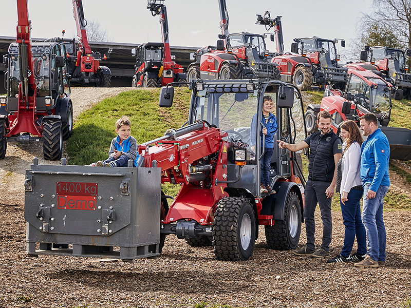 Personengruppe bei Traktor-Demonstration mit 1400 kg Ladegewicht in einem Freigelände.