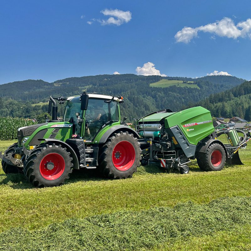 Ein grüner Fendt 516 Traktor mit einer angehängten Fendt Rotana F130 Ballenpresse auf einem Feld.