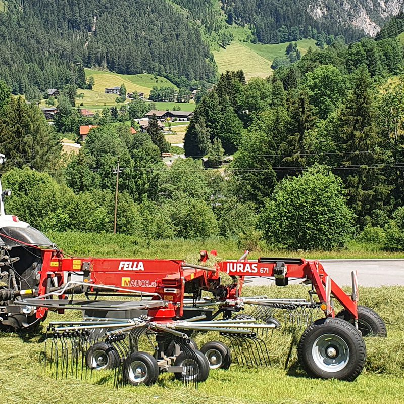 Heumaschine Fella Juras 671 auf einem Feld vor einer Waldlandschaft.