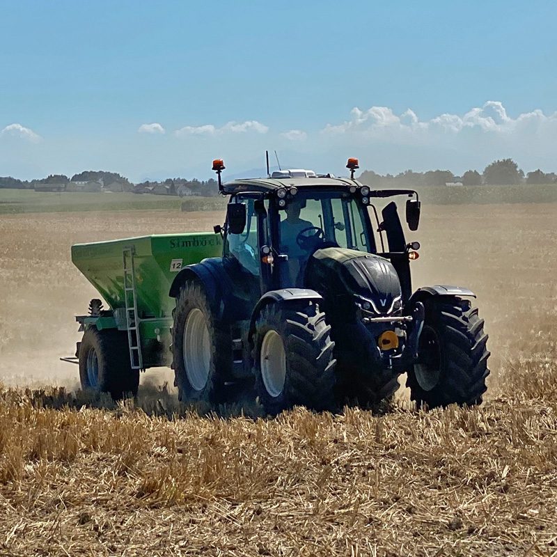 Traktor Valtra N175 Direct mit einem Anhänger von Simplock fährt über ein trockenes Feld.