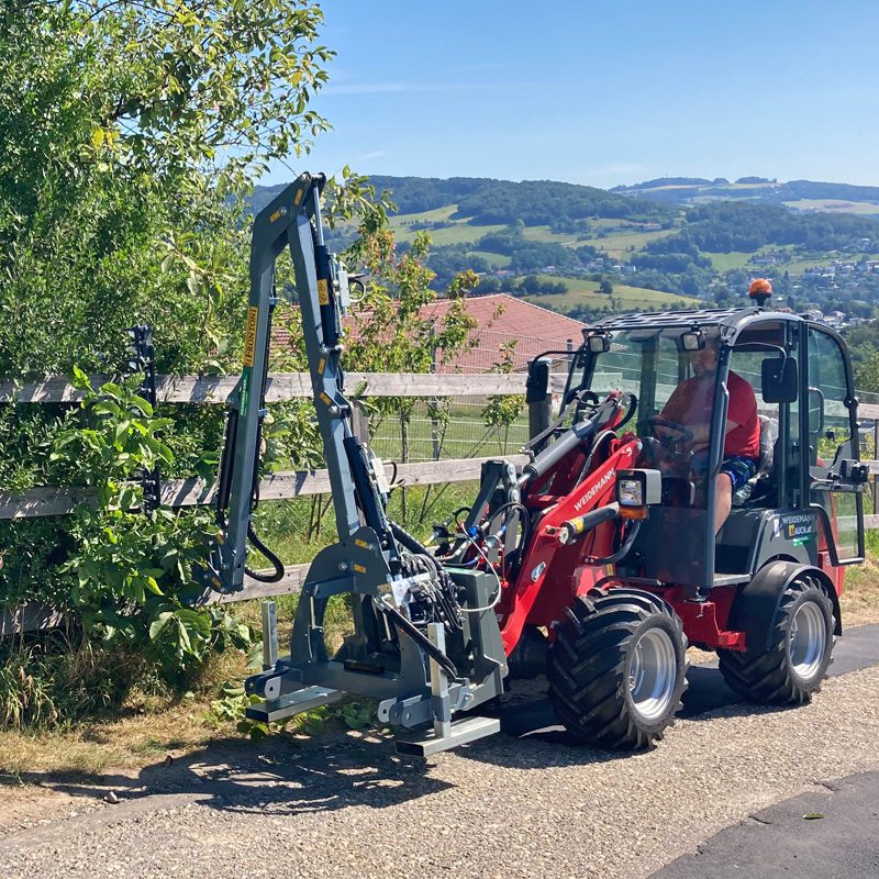 Ein Weidemann-Radlader mit Frontonie-Spider-150-Hackgerät auf einem ländlichen Weg.