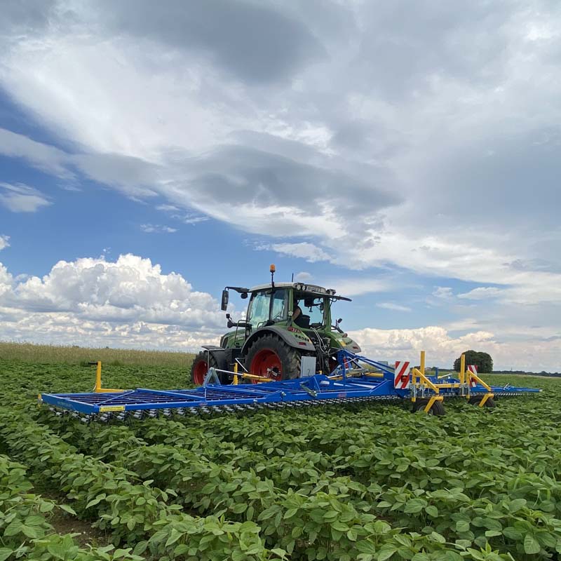 Traktor mit Treffler-Maschine arbeitet auf einem Feld unter wolkigem Himmel.