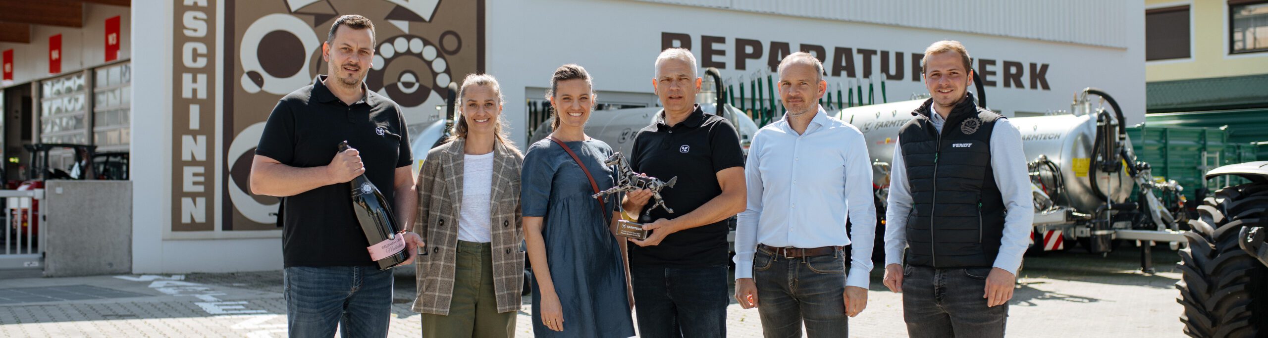 Sechs lächelnde Personen stehen vor einem Maschinen Reparaturwerk-Schild und halten verschiedene Gegenstände.