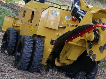 Tăietor de cioturi_358x265px Mașină de tocat cioturi galbenă în uz pe o zonă forestieră neuniformă.